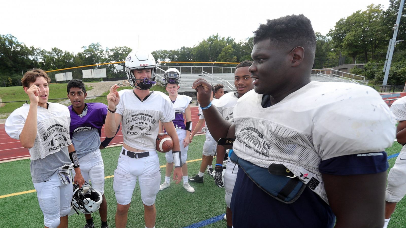 PHOTO: Bloomfield Hills' Dean Bolton, Santhosh Ramachandran and Tasnner Slazinski sign with Bloomfield Hills defensive lineman Devin Holmes, right, who is deaf, during practice on Wednesday, Sept. 4, 2019, at Bloomfield Hills High School.