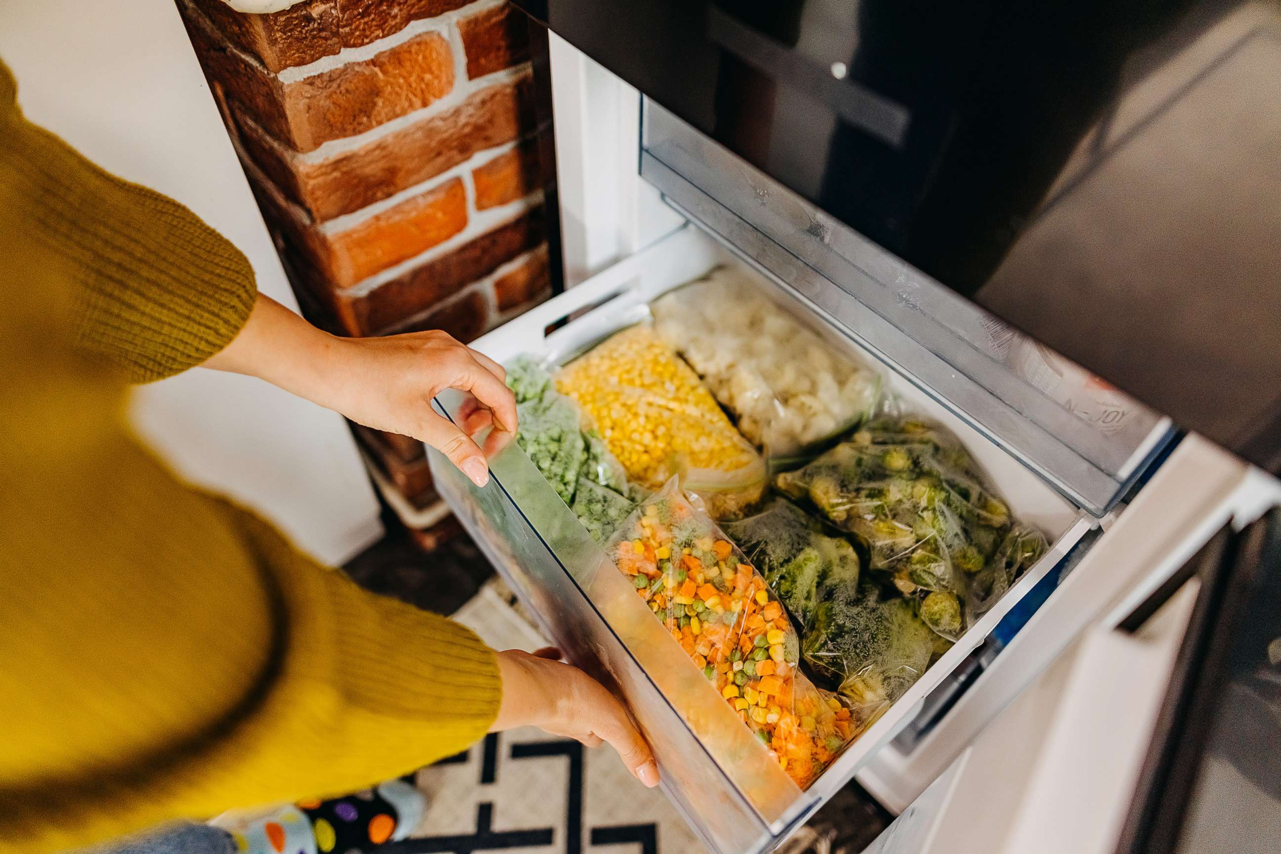 PHOTO: Woman putting container with frozen mixed vegetables to refrigerator