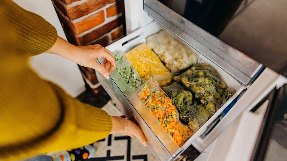 PHOTO: Woman putting container with frozen mixed vegetables to refrigerator