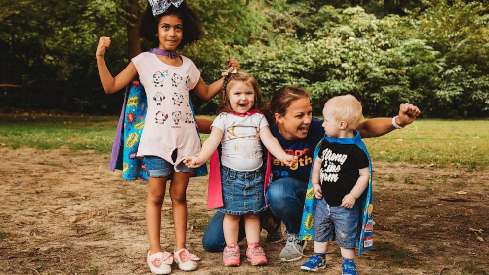 PHOTO: CEO Robyn Rosenberger takes a photo with three Tiny Superheroes.