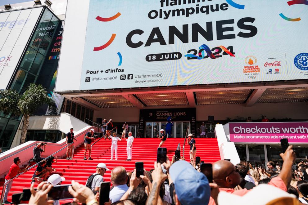 PHOTO: Actress Halle Berry (L) and Thierry Fremaux carry the Olympic Torch in front of the Palais des Festivals during the Cannes Lions International Festival Of Creativity 2024 - Day Two on June 18, 2024 in Cannes, France.