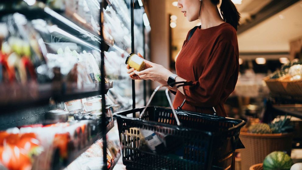 PHOTO: A woman shopping for groceries examines a food label while holding a shopping basket in an undated stock image.