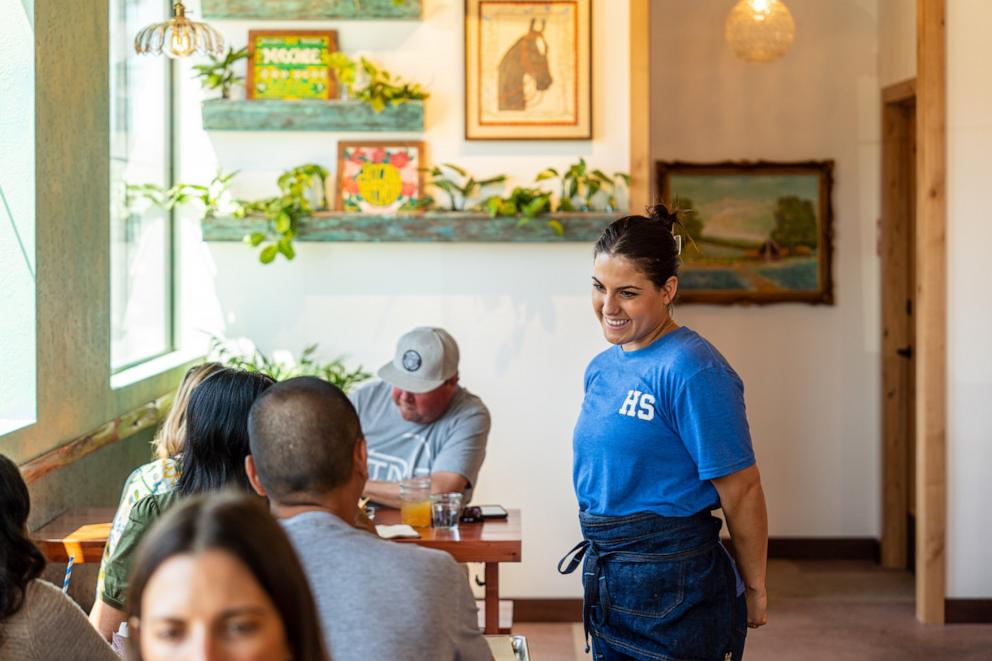 PHOTO: A server at HomeState in Oceanside, California talks with customers seated at a table.