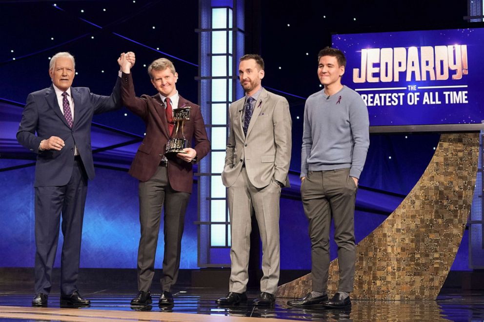 PHOTO: Jeopardy! Greatest of All Time tournament championship winner Ken Jennings raises his hand in victory alongside host Alex Trebek and fellow competitors, Brad Rutter and James Holzhauer.