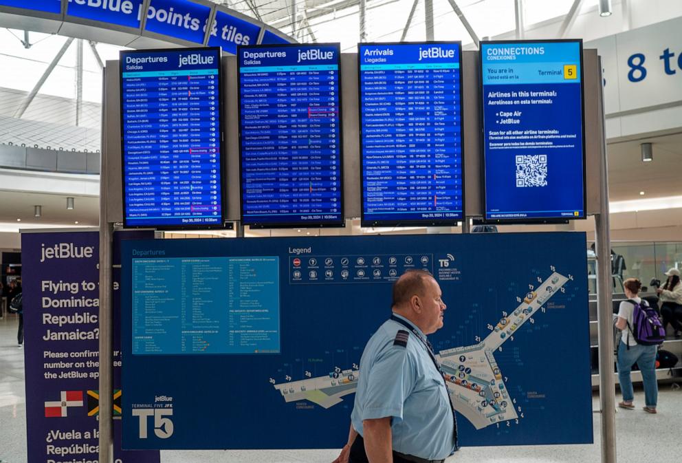 PHOTO: A JetBlue Airways pilot walks past a departure-arrival board September 30, 2024 at JFK International Airport in New York City.