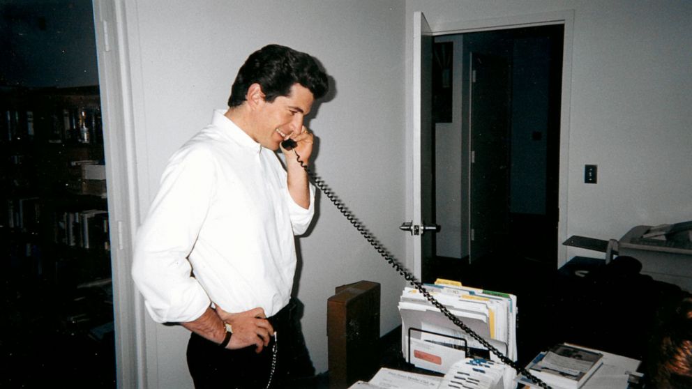 PHOTO: John F. Kennedy Jr. talks on the phone at the desk of his chief of staff RoseMarie Terenzio.