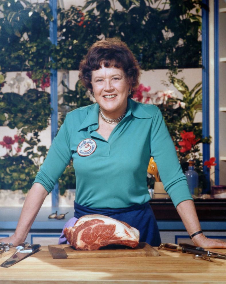 PHOTO: Chef Julia Child standing with a cut of meat in her kitchen.