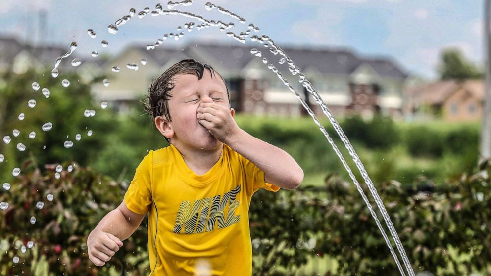 PHOTO: Owen Boarman, 3, holds his nose as he runs through water spray on a hot day, July 17, 2019, in Owensboro, Ky.