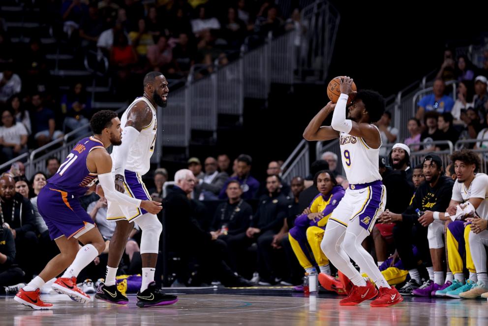 PHOTO: Bronny James #9 of the Los Angeles Lakers shoots against Tyus Jones #21 of the Phoenix Suns as teammate LeBron James #23 looks on during the second quarter at Acrisure Arena on October 06, 2024 in Palm Springs, California.