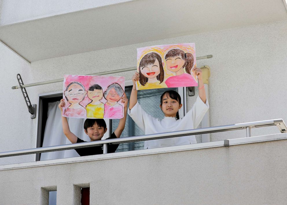 PHOTO: Reku Matsui, 8, and Yaya Matsui, 12, pose for a photograph while holding pictures that they drew during the coronavirus disease (COVID-19) outbreak, as they stand on the balcony of their home in Tokyo, April 19, 2020.