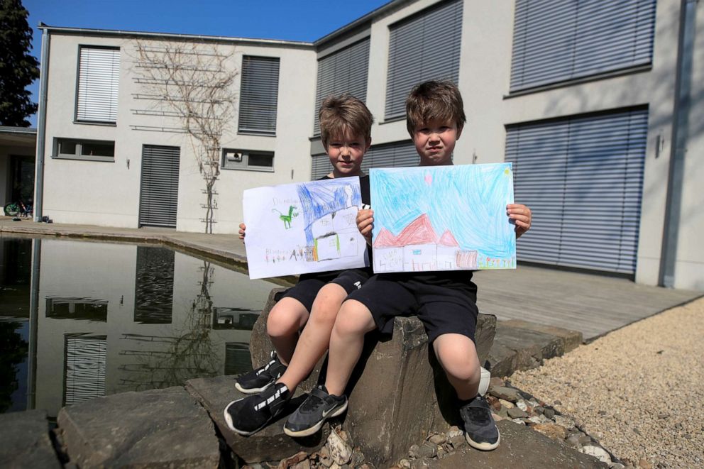 PHOTO: Noa, 7, and Tom, 6, pose for a photograph while holding pictures that they drew during the coronavirus disease (COVID-19) outbreak, as they sit in front of their house in Bad Honnef, Germany, April 17, 2020. 