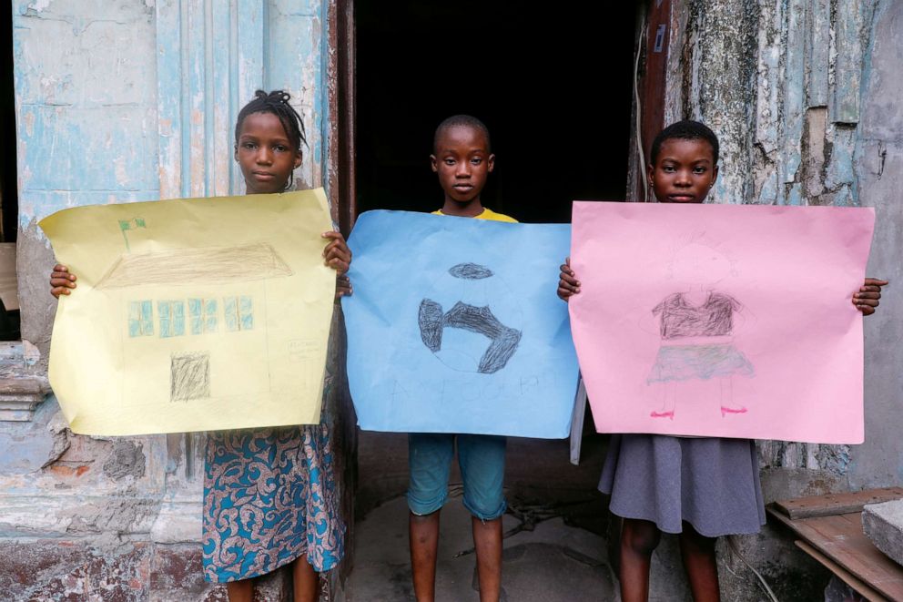PHOTO: Sofiat Kolawole, 8, Olatunji Adebayo, 11, and Amira Akanbi 11, pose for a photograph while holding pictures that they drew during the coronavirus disease (COVID-19) outbreak, as they stand in front of their house in Lagos, Nigeria, April 18, 2020.