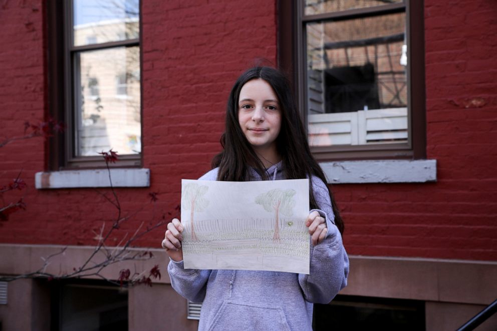 PHOTO: Jane Hassebroek, 13, poses for a photograph while holding a picture that she drew during the coronavirus disease (COVID-19) outbreak, while standing outside her home in Brooklyn, New York, April 19, 2020.