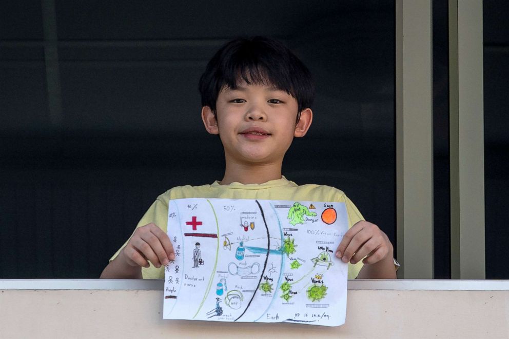 PHOTO: Nipoon Kitkrailard, 10, poses for a photograph while holding a picture that he drew during the coronavirus disease (COVID-19) outbreak, as he stands by a window at his home in Samut Prakan, Thailand, April 21, 2020.