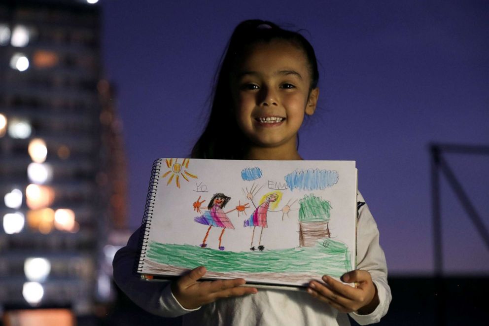 PHOTO: Matilda Soto Quilenan, 6, poses for a photograph while holding a picture that she drew during the coronavirus disease (COVID-19) outbreak, as she stands on the roof of her house, in Santiago, Chile, April 20, 2020.