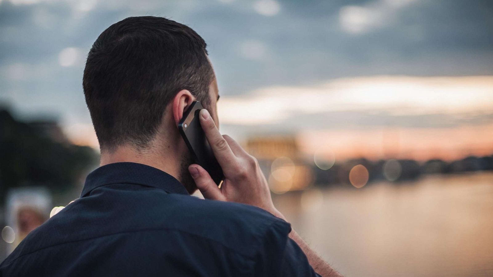 PHOTO: Businessman talking on mobile phone at sunset looking at evening city