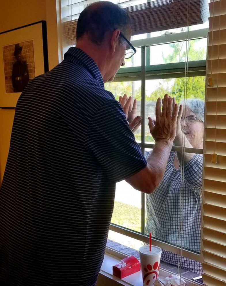 PHOTO: Mary Daniel and her husband Steve join hands through a window after the novel coronavirus pandemic suspended in-person visitations at the Rosecastle Assisted Living and Memory Care facility in Jacksonville, Fla.
