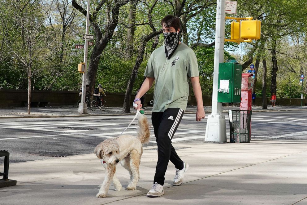 PHOTO: A man wearing a bandana as a face covering walks a dog during the coronavirus pandemic, April 28, 2020, in New York.
