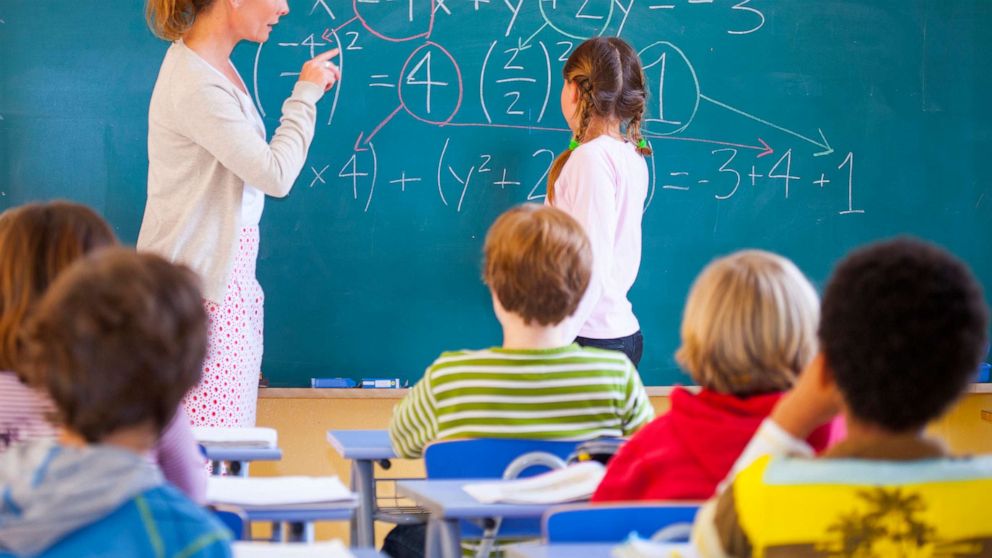 PHOTO: A teacher helps a student with a math problem in a classroom. 