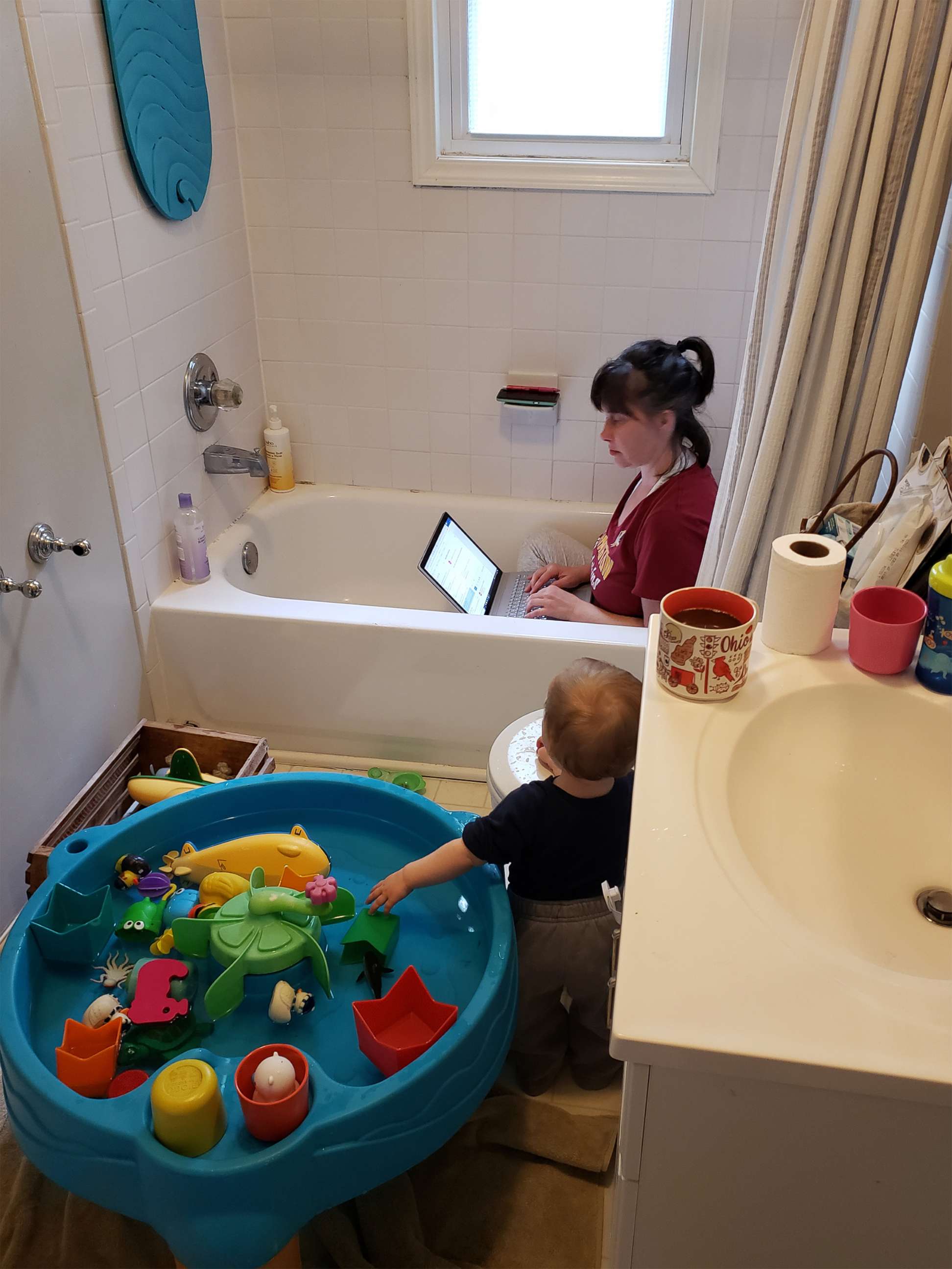 PHOTO: Heidi Lewis, a mother of two, is seen working from home in Silver Spring, Maryland, amidst in-person child care and school closures, April 2020. Her 1-year-old daughter Harriet is seen playing beside her in the bathroom.