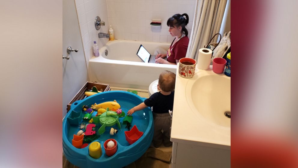 Heidi Lewis, a mother of two, is seen working from home in Silver Spring, Maryland, amidst in-person child care and school closures, April 2020. Her 1-year-old daughter Harriet is seen playing beside her in the bathroom.