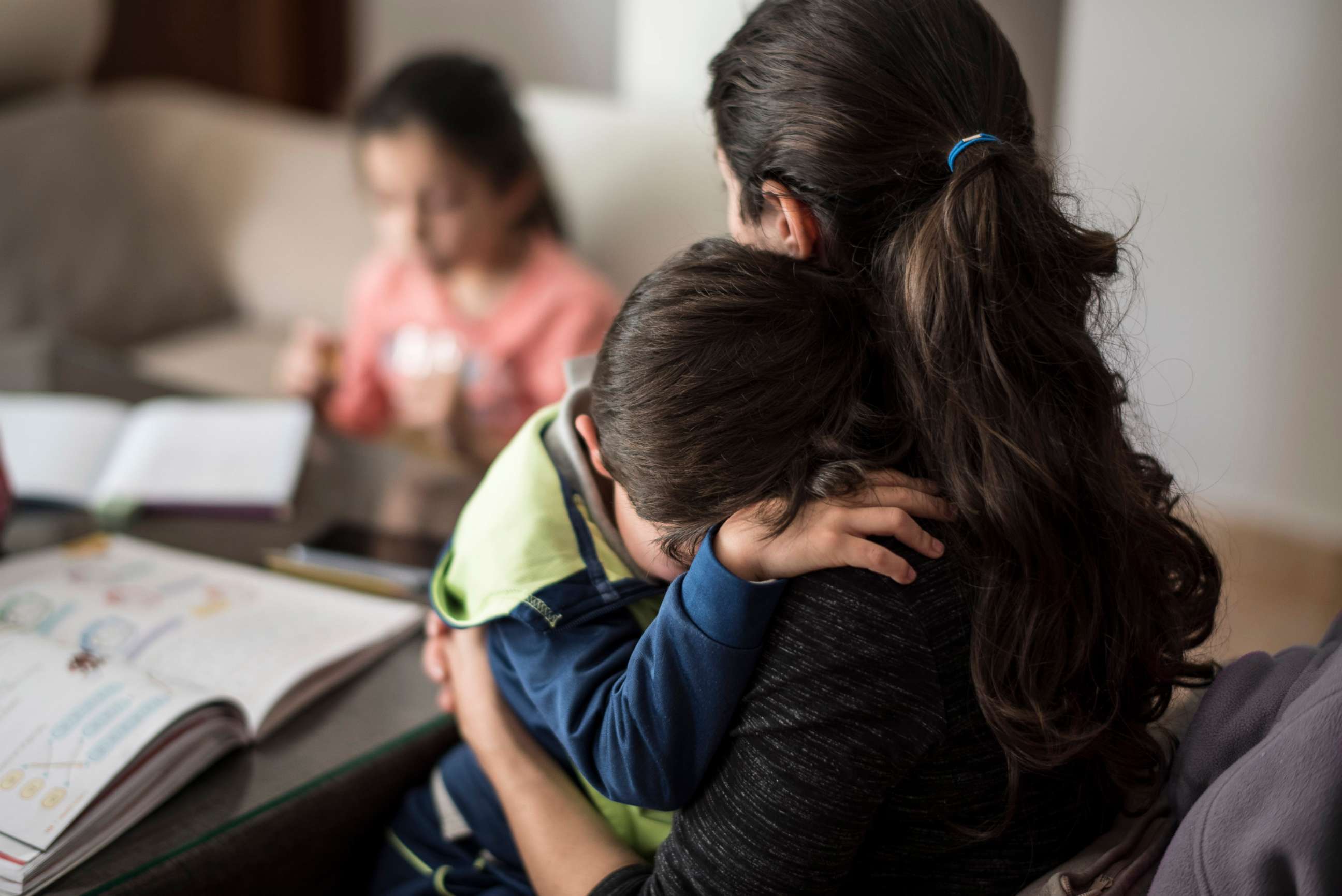 PHOTO: A mother comforts her crying son while in the background her daughter performs homework.