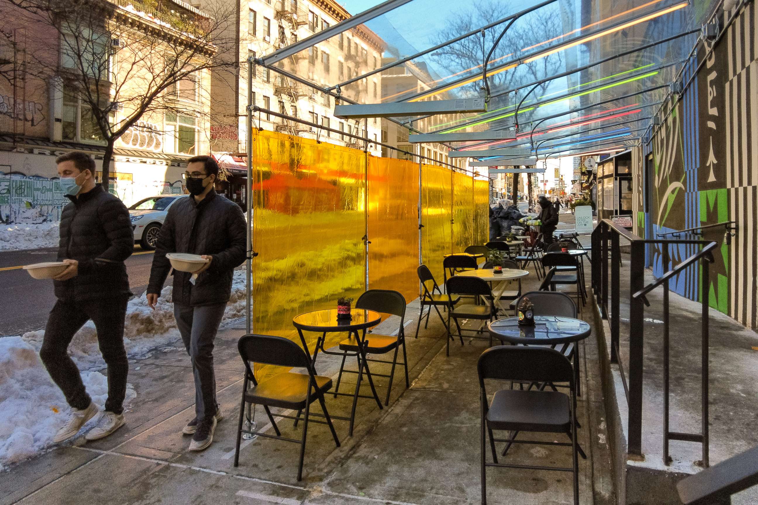 PHOTO: People holding takeout meal orders walk past an outdoor dining area in the Nolita neighborhood of Manhattan during the coronavirus pandemic on Feb. 04, 2021, in New York.