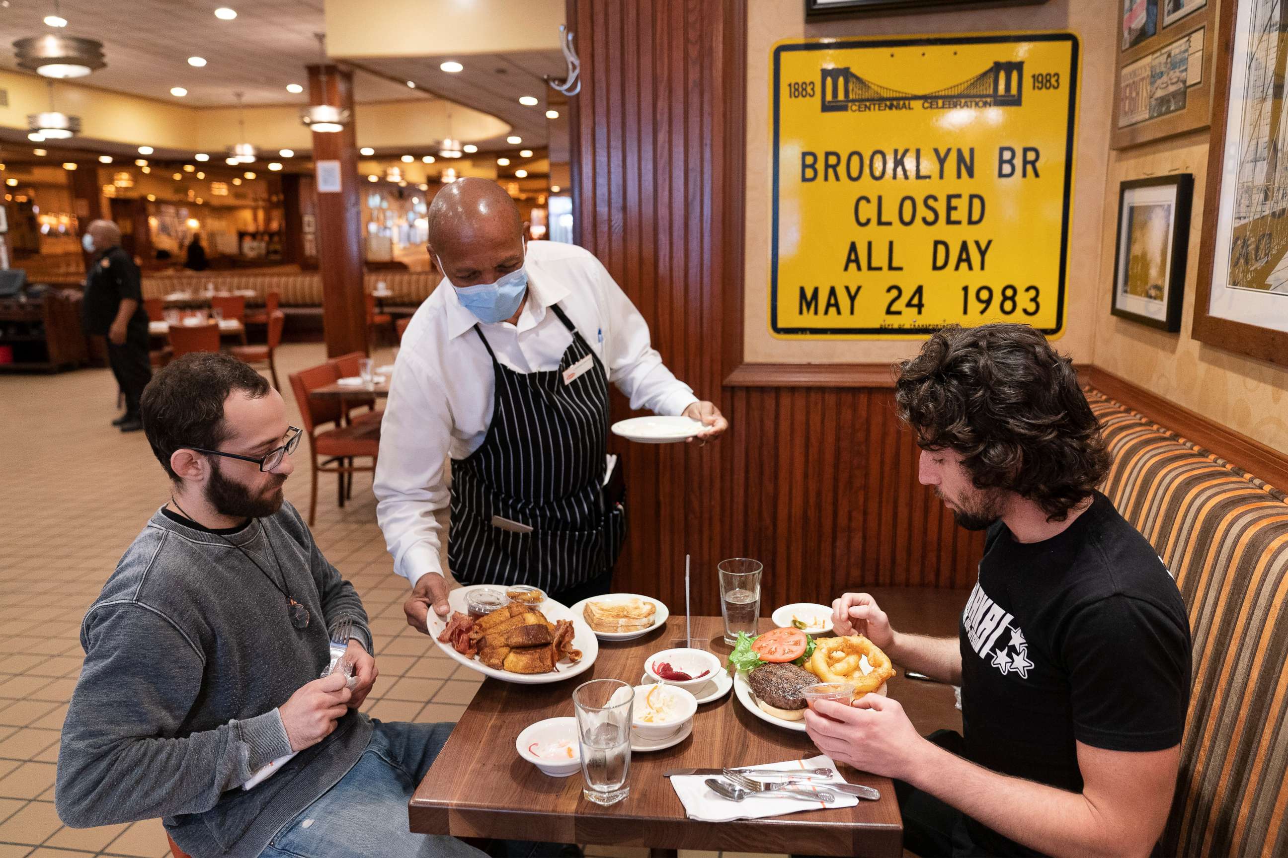 PHOTO: Lenworth Thompson serves lunch to David Zennario, left, and Alex Ecklin at Junior's Restaurant in New York, Sept. 30, 2020.