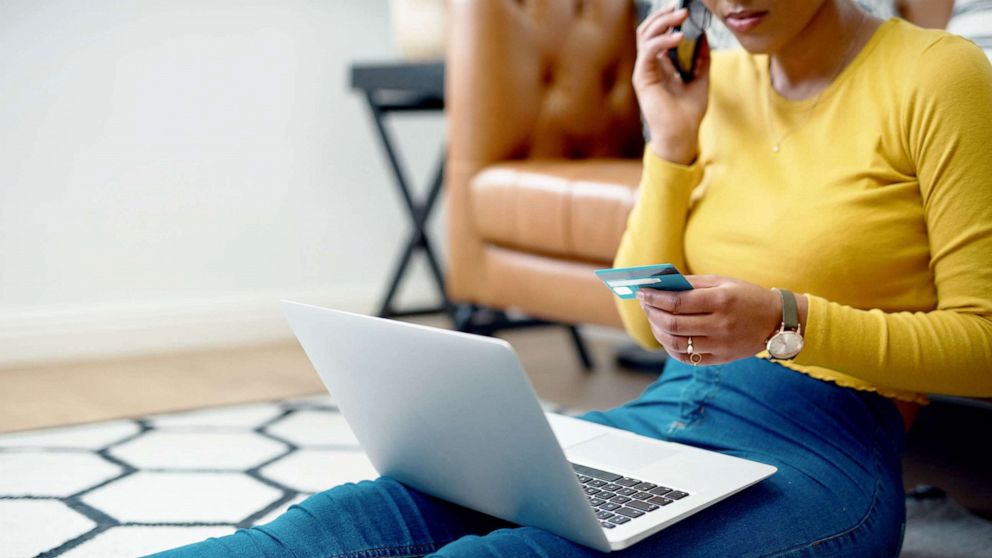 PHOTO: A woman shops online with a laptop and smartphone as she sits on the floor in an undated stock image.