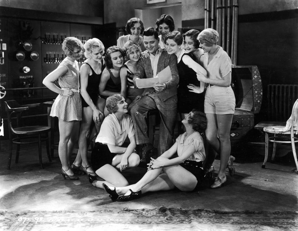 PHOTO: American actor Charles King (1889 - 1944) reads to a group of chorus girls gathered around him in a still from the film, 'The Broadway Melody,' directed by Harry Beaumont. 