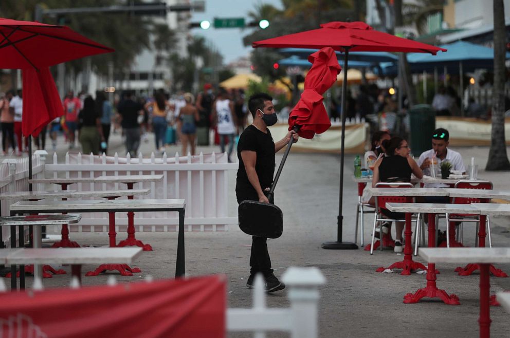 PHOTO: A worker at the Boulevard Hotel restaurant carries an umbrella in the outdoor seating area of a restaurant in Miami Beach, Fla., July 18, 2020.