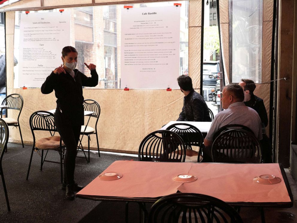 PHOTO: A waitress explains the combined menus from B44 Catalan Bistro and Cafe Bastille French Bistro to their first customers during San Francisco's first day of reopening for restaurants and outdoor dinning only in San Francisco, June 12, 2020.
