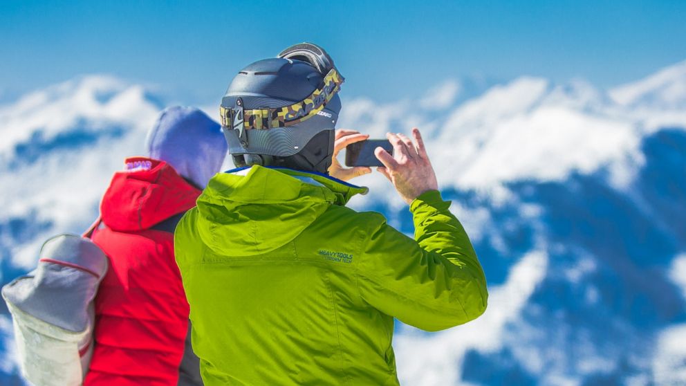 PHOTO: Man in Green Jacket and Gray Helmet Holding Phone Standing Next to Person in Red and Black Jacket