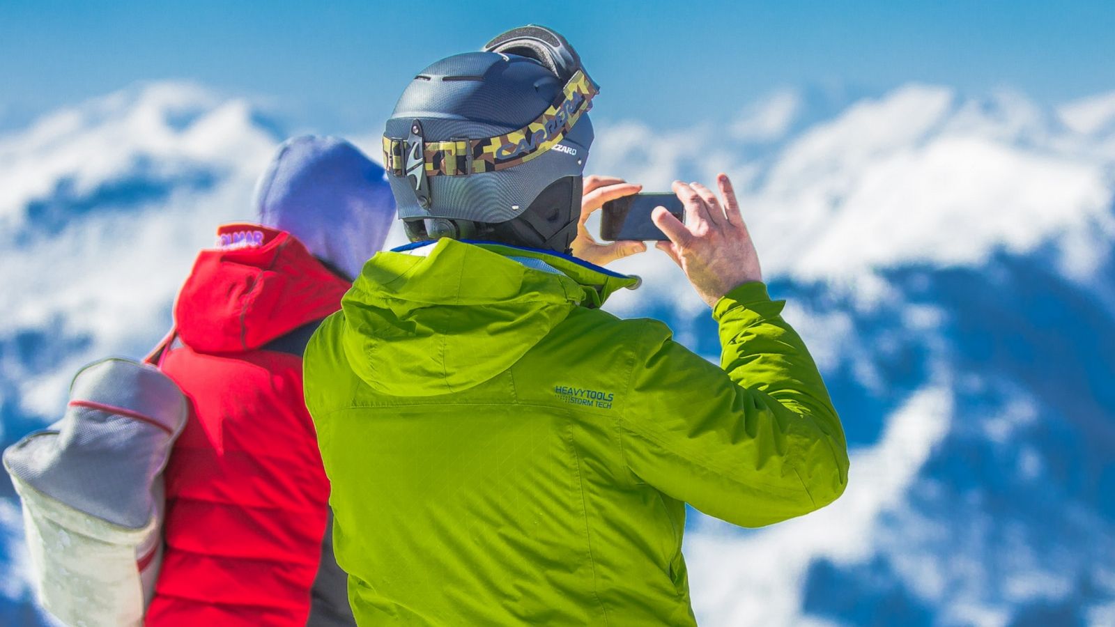 PHOTO: Man in Green Jacket and Gray Helmet Holding Phone Standing Next to Person in Red and Black Jacket