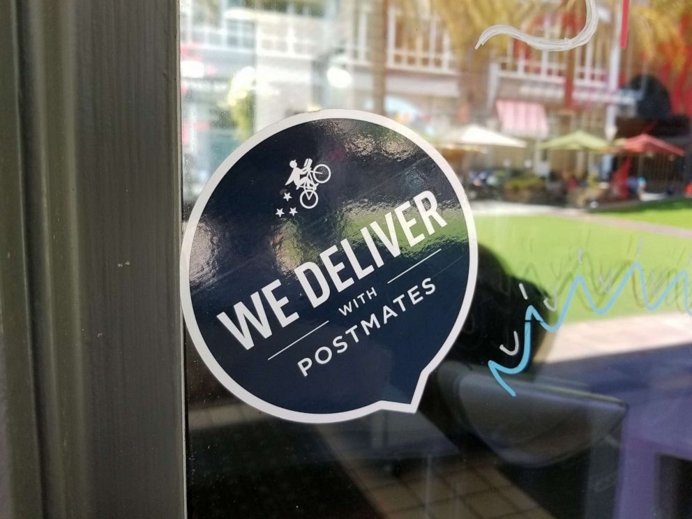 PHOTO: Close-up of logo reading We Deliver With Postmates, referencing the Postmates food delivery app service, on a restaurant window in San Jose, Calif., June 7, 2018.