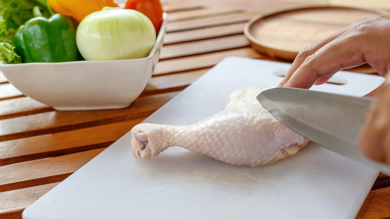 PHOTO: A person cuts raw poultry on a cutting board.