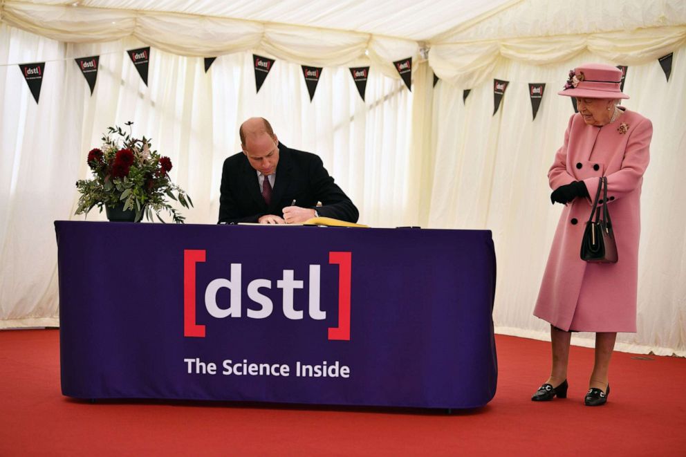 PHOTO: Britain's Queen Elizabeth II (R) stands by as Britain's Prince William, Duke of Cambridge (L) signs a visitor's book during their visit at Porton Down science park near Salisbury, southern England, on Oct. 15, 2020.