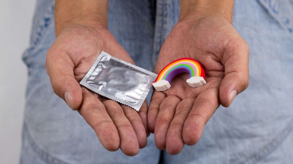 PHOTO: A person holds a rainbow trinket and a condom in their hands.