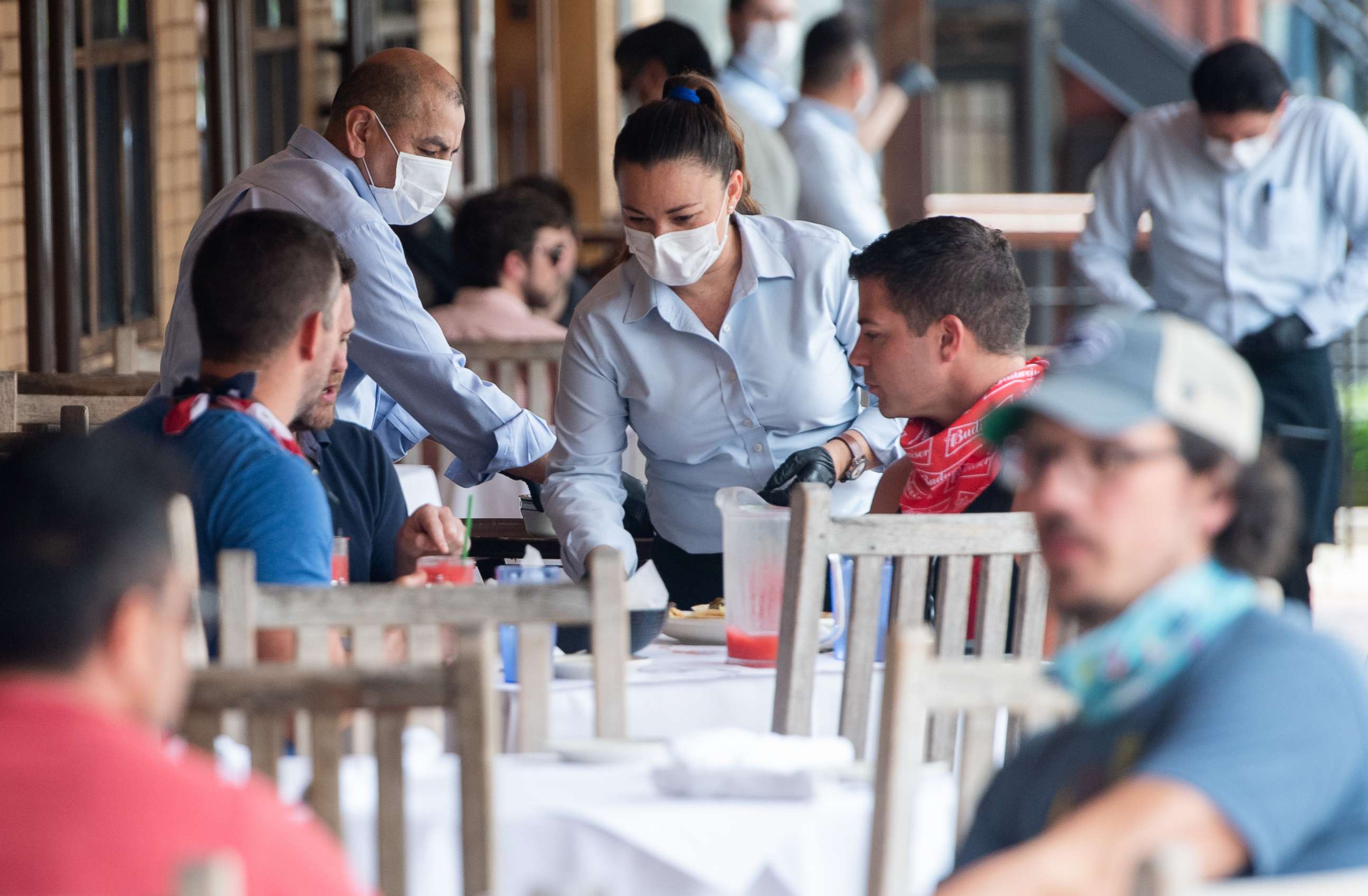 PHOTO: A waiter wearing a mask and gloves delivers food to a table to customers seated at an outdoor patio at a Mexican restaurant in Washington, D.C., May 29, 2020.