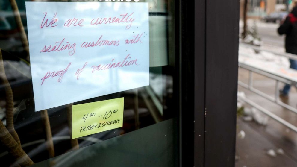 PHOTO: A sign in the window at Bar Max reads, We are currently seating customers with proof of vaccination, on April 16, 2021, in Denver.