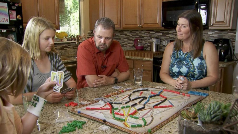 PHOTO: Carl and Mindy Jensen play a board game with their two children.