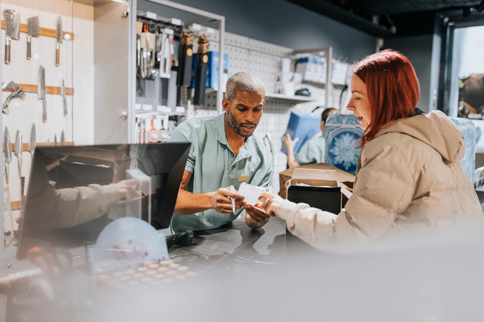 PHOTO: Male retail clerk showing bill to female customer at checkout in electronics store