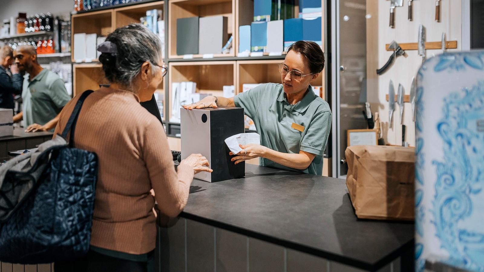 PHOTO: Female sales clerk giving appliance box to customer at checkout counter in electronics store