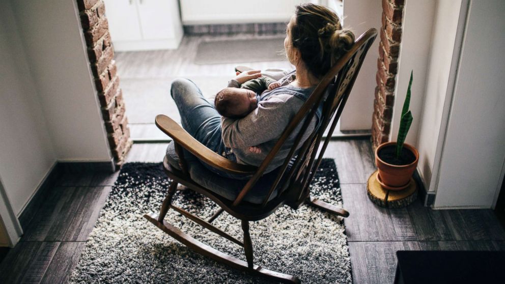 In this undated stock photo, a young mother in a rocking chair rocks her newborn baby to sleep.