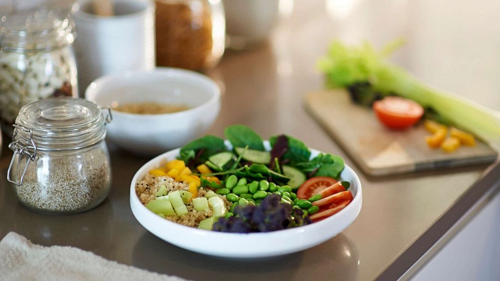 PHOTO: A vegan salad bowl of quinoa, peppers, spinach, soya beans, tomatoes, cucumber, purple sprouting broccoli is placed on a kitchen counter. 