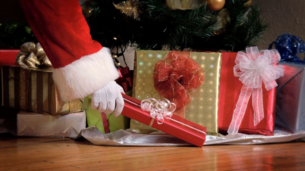 PHOTO: Santa puts a gift under a Christmas tree.