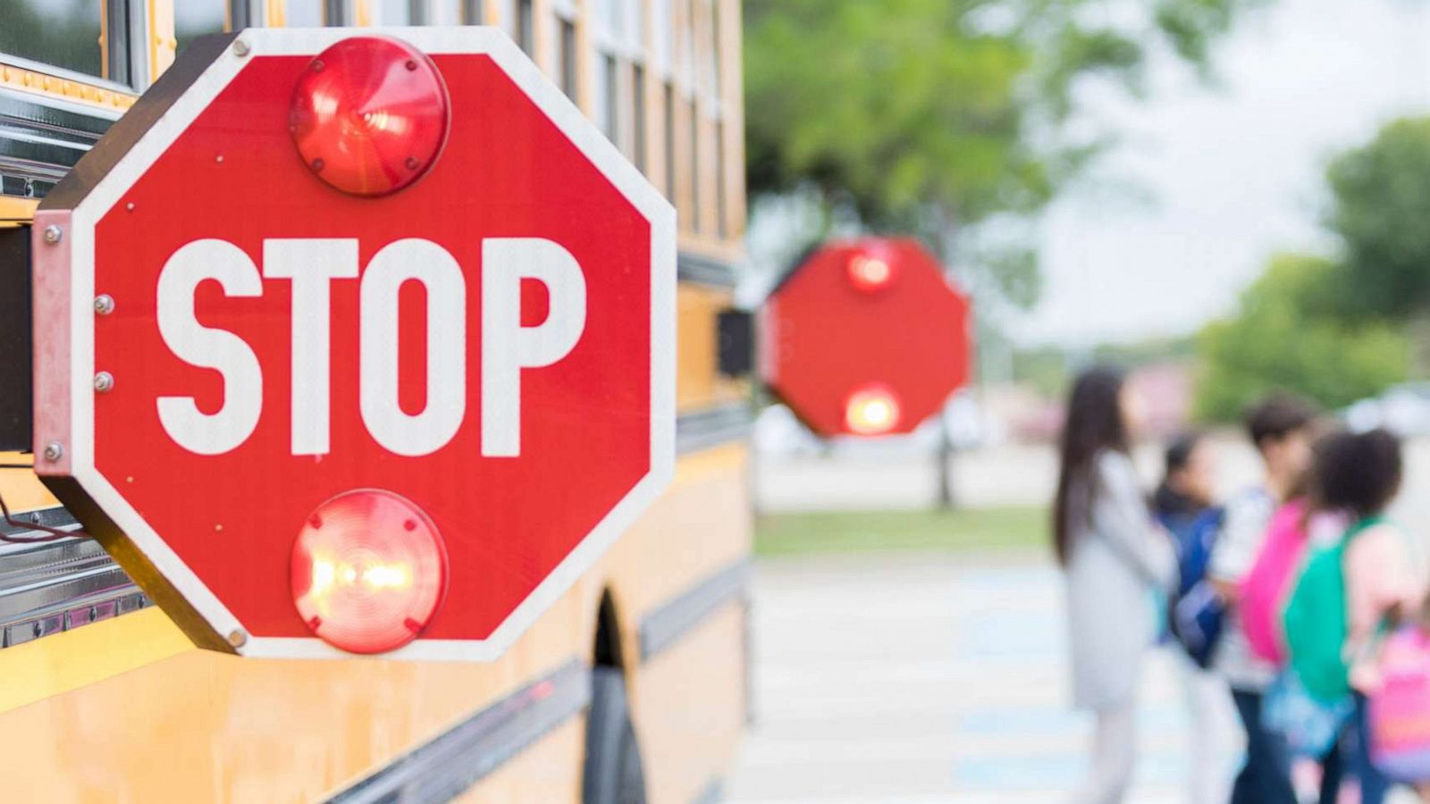 PHOTO: Close up of stop sign on school bus as children cross the street in the background.