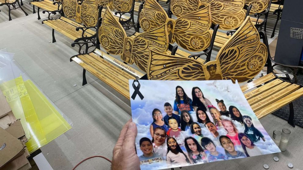 PHOTO: Sean Peacock holds a photo of the 21 victims of the Robb Elementary School shooting in front of the memorial benches he made in their honor.