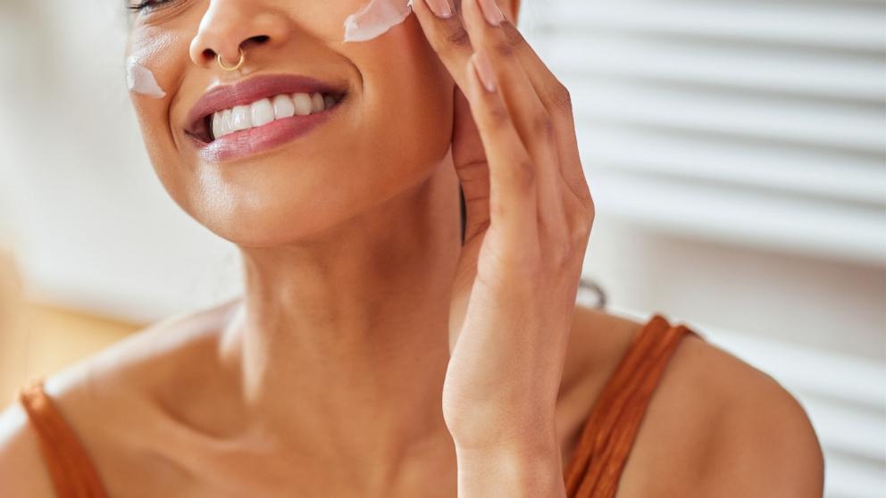 PHOTO: A woman puts lotion on her face in the mirror.