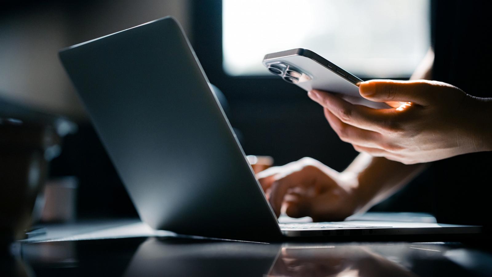 PHOTO: Stock photo of a person using their phone and laptop.